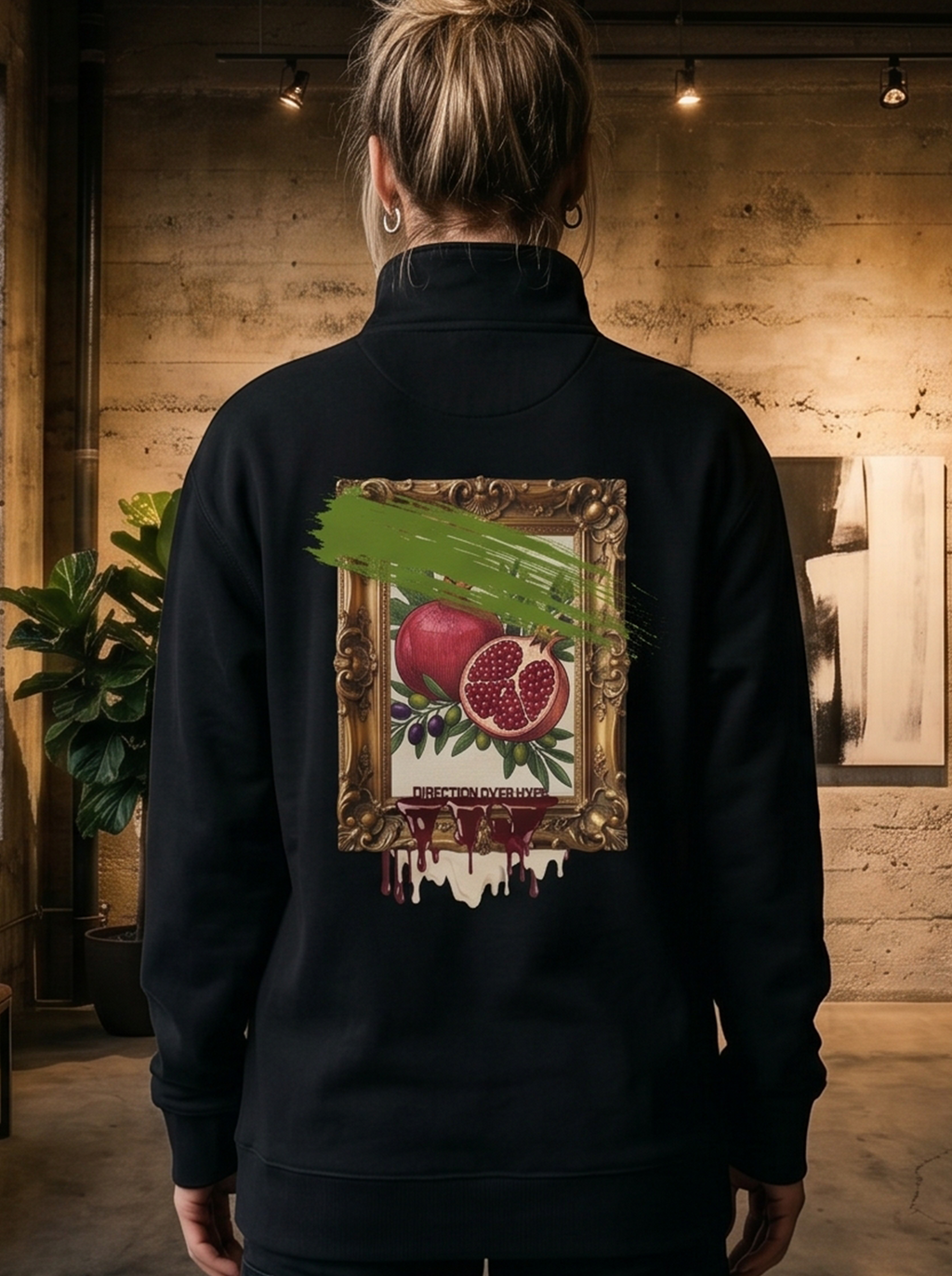 Person wearing a black jacket with a painting of pomegranates on the back, standing in an art gallery.