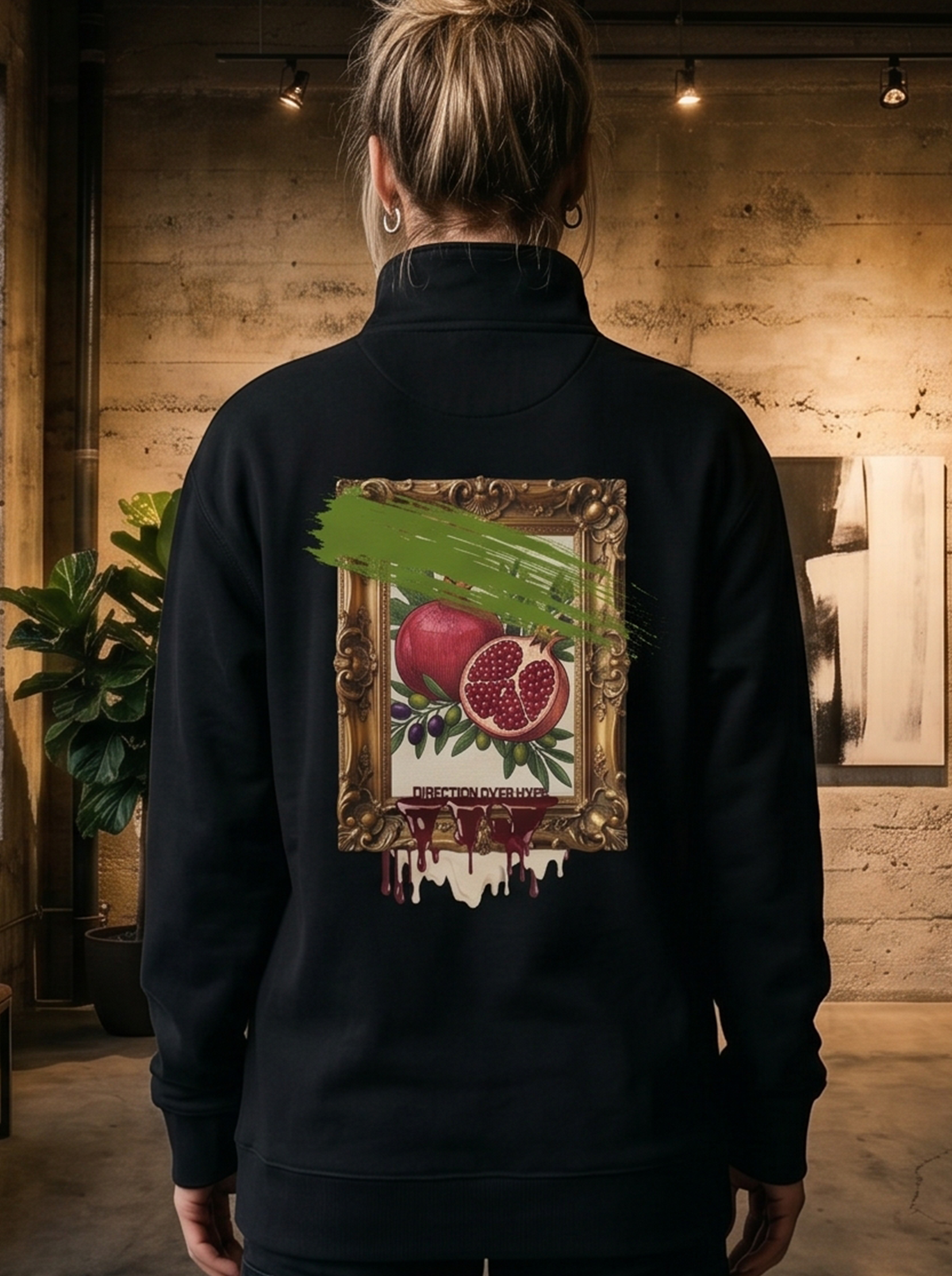 Person wearing a black jacket with a painting of pomegranates on the back, standing in an art gallery.