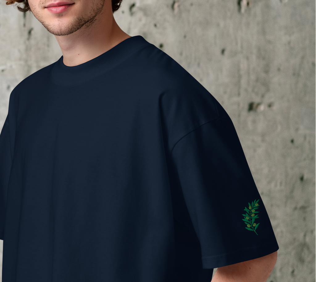 Man wearing a navy blue t-shirt with a green embroidered olive branch against a concrete wall.